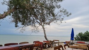 A beachside café with wooden tables and chairs, a blue umbrella, and a view of the sea. - Rungarun Resort (Chaiya)