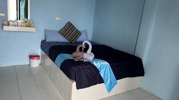 A single bed with a blue and black bedspread, a striped pillow, and a towel shaped like a swan. A small trash bin is visible to the left.