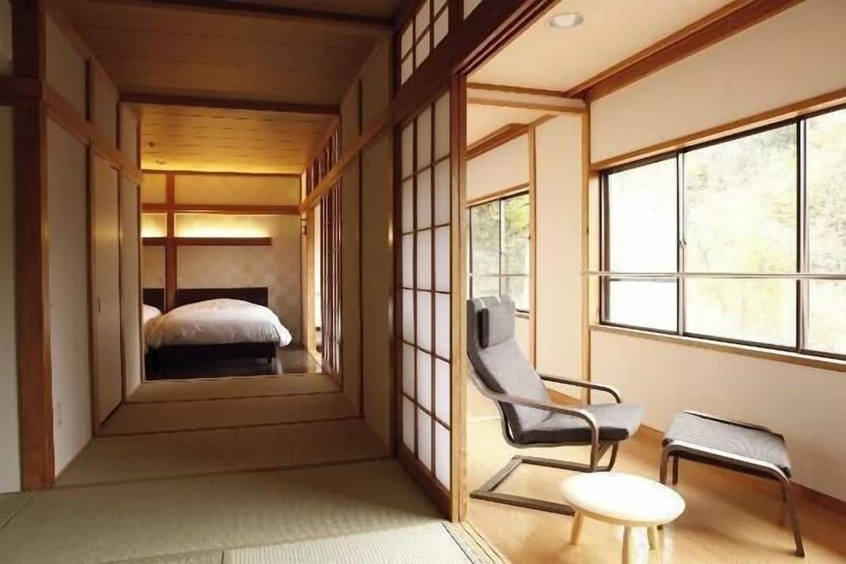 Una habitación japonesa tradicional con suelo de tatami, un futón, puertas correderas shoji y vistas a través de un gran ventanal.