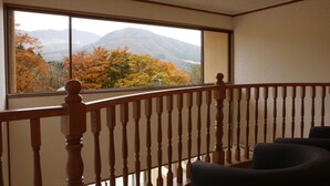 A room with a wooden balcony railing, a large window offering a view of autumn trees and mountains. - Hakone Fura (Hakone)