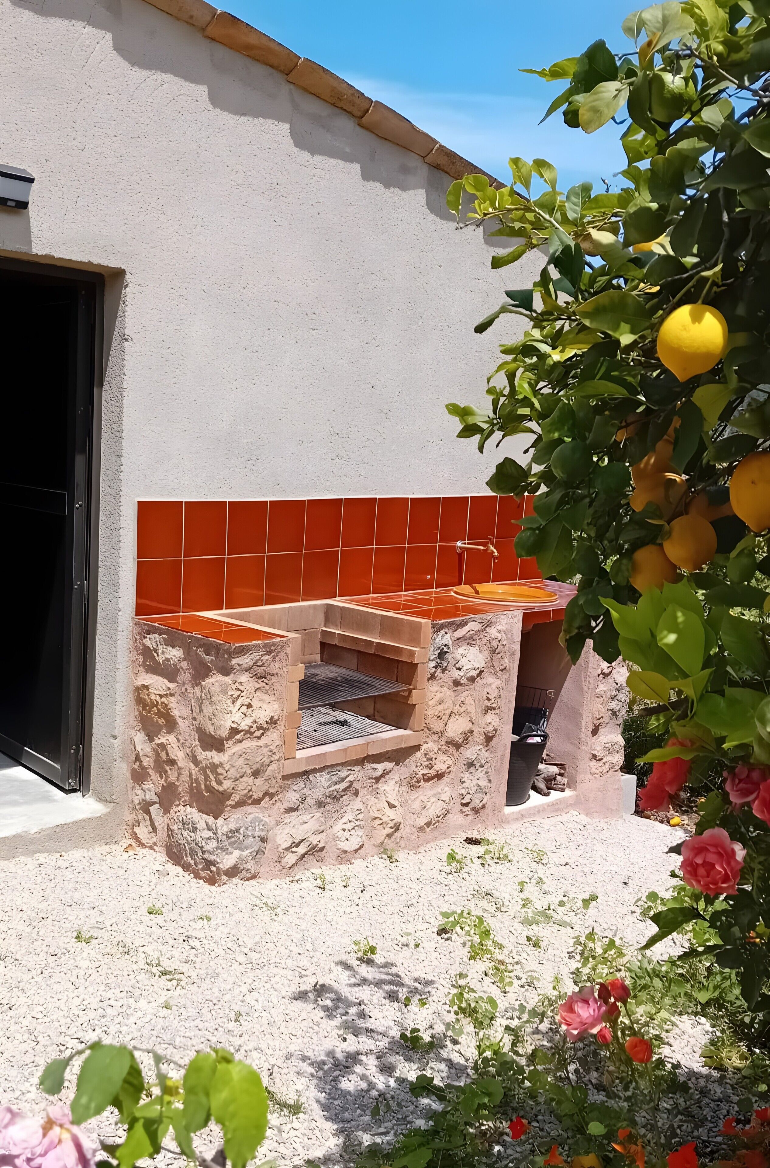 Cocina exterior de piedra con baldosas anaranjadas, un fregadero y una parrilla.