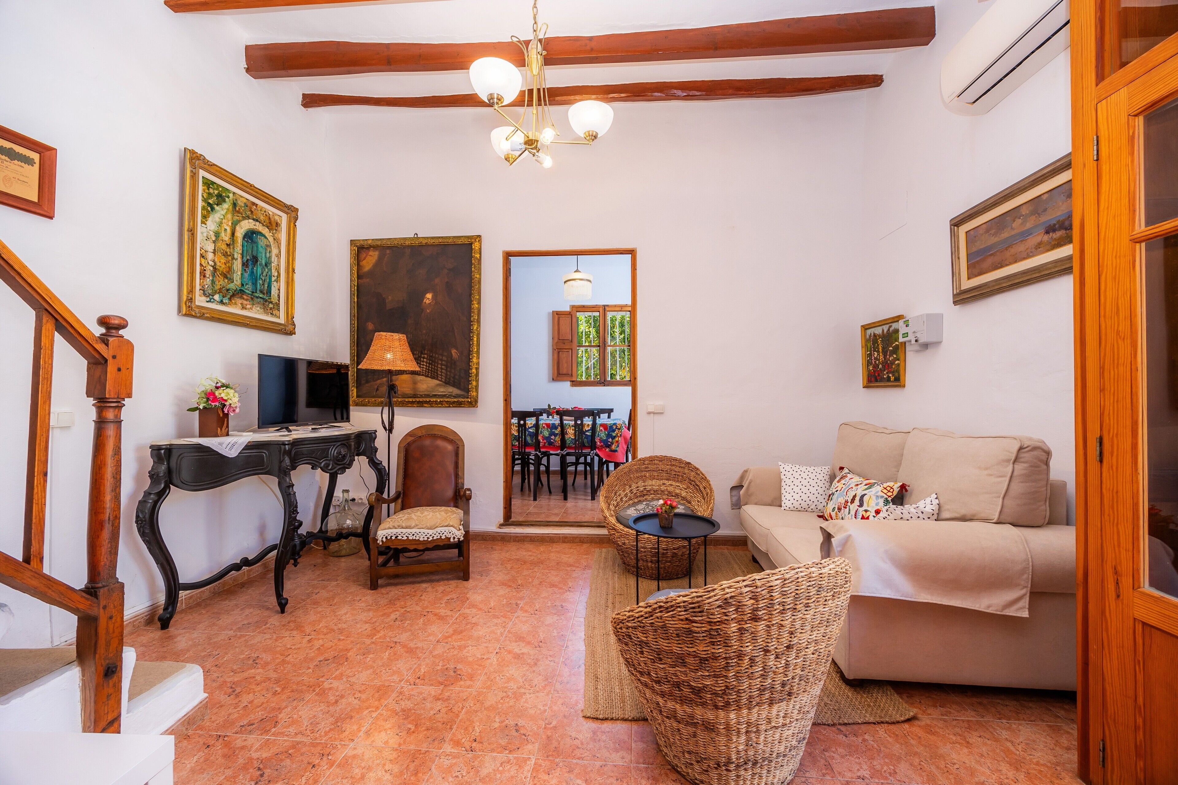 A living room with a sofa, wicker chairs, a table, a TV, and artwork on the walls.