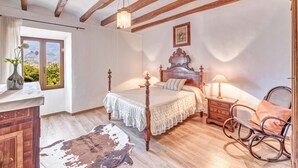 Quarto com cama de madeira, uma cadeira de balanço, mesa de cabeceira e janela com vista.