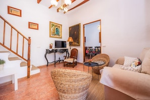 Una sala de estar con una escalera, televisor, sillón, sofá y espejo.