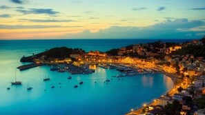 Un pueblo costero al atardecer con un puerto deportivo, edificios y un faro.
