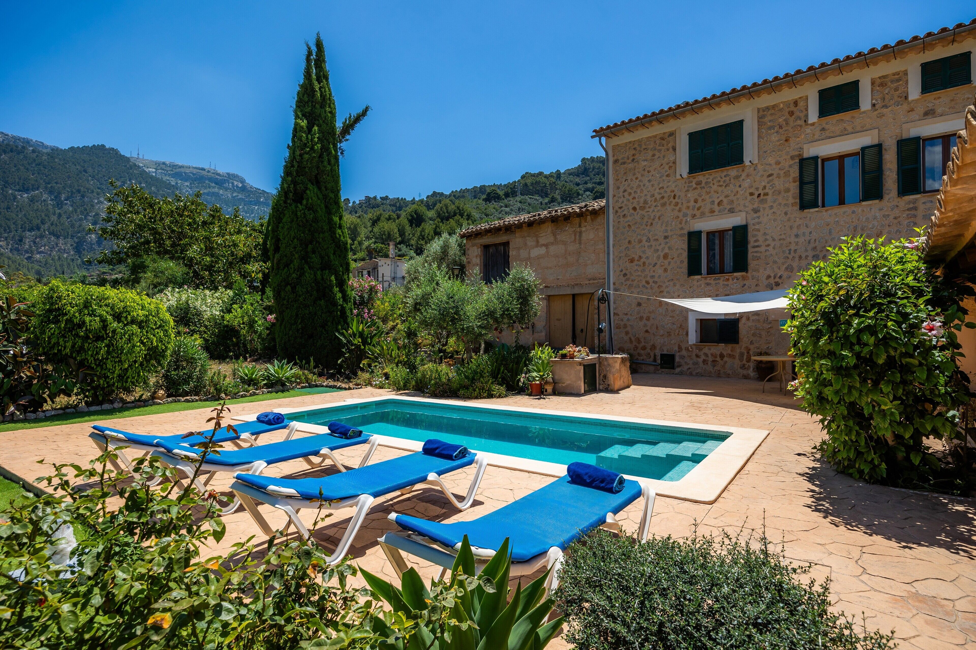 Un espace piscine avec des chaises longues, un bâtiment en pierre et une végétation luxuriante tout autour.