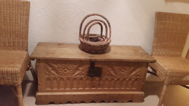 A wooden chest with floral carvings, a woven basket on top, and wicker chairs. - Vacation flat in idyllic location — Casa Ogna (Klosters)