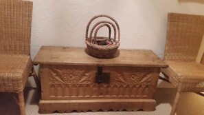 A wooden chest with floral carvings, a woven basket on top, and wicker chairs.