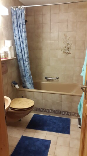A bathroom with a bathtub, toilet, and shower curtain.