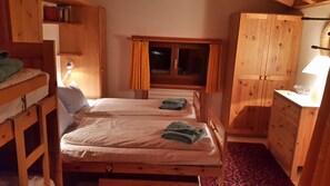 A wooden room with two beds, a window, and a wooden wardrobe.