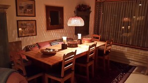 A dining room with a wooden table, chairs, a decorative lamp, and framed pictures on the wall. - Vacation flat in idyllic location — Casa Ogna (Klosters)
