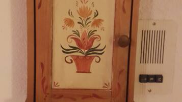 Un armadietto in legno con decorazioni floreali, uno sportello e un termostato fissato alla parete.