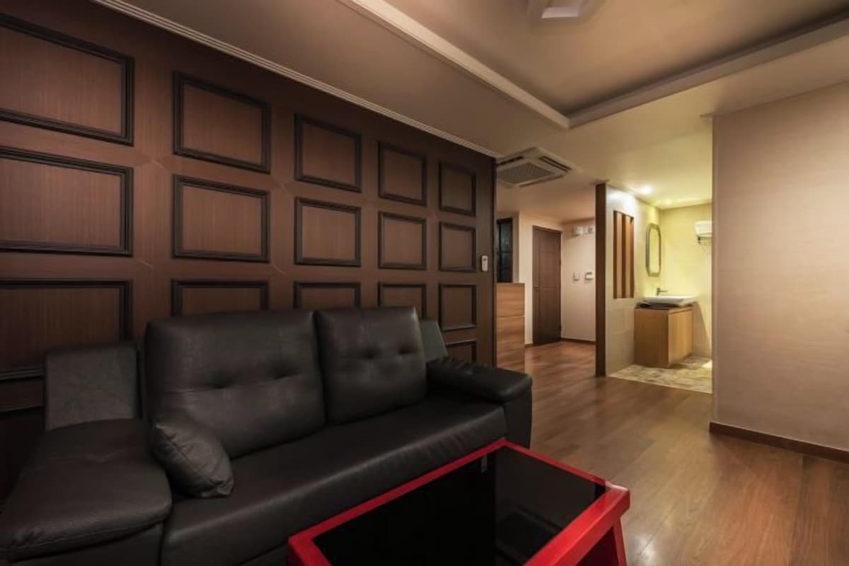 Una sala de estar moderna con un panel de pared marrón oscuro, un sofá de cuero negro y una mesa de centro con marco rojo.