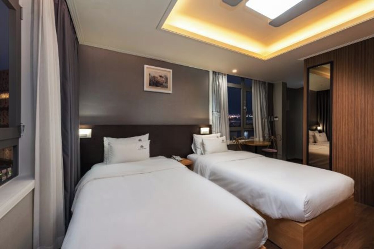 Habitación de hotel con dos camas, un espejo grande y vista a la ciudad de noche.