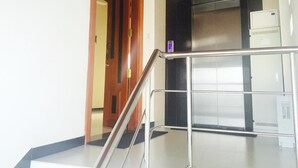 Un interior moderno con barandilla de vidrio, puerta de madera y ascensor de acero inoxidable.