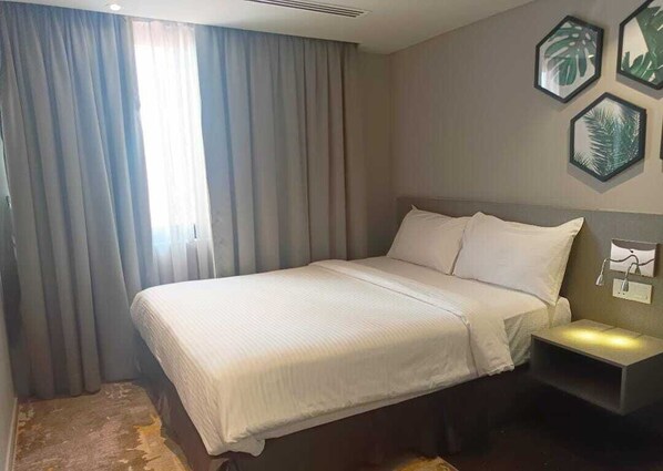 A hotel room with a bed, curtains, a nightstand, and framed wall art.