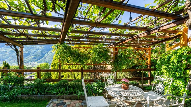 A garden patio with a pergola, white metal chairs, and a table with a flower pot. - Holiday Apartment "Casa Margherita" in Idyllic Location (Aosta)