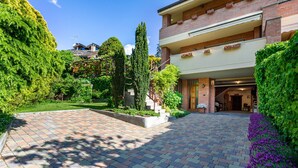 A paved courtyard with a brick pathway, a multi-level building with a balcony, and lush greenery. - Holiday Apartment "Casa Margherita" in Idyllic Location (Aosta)