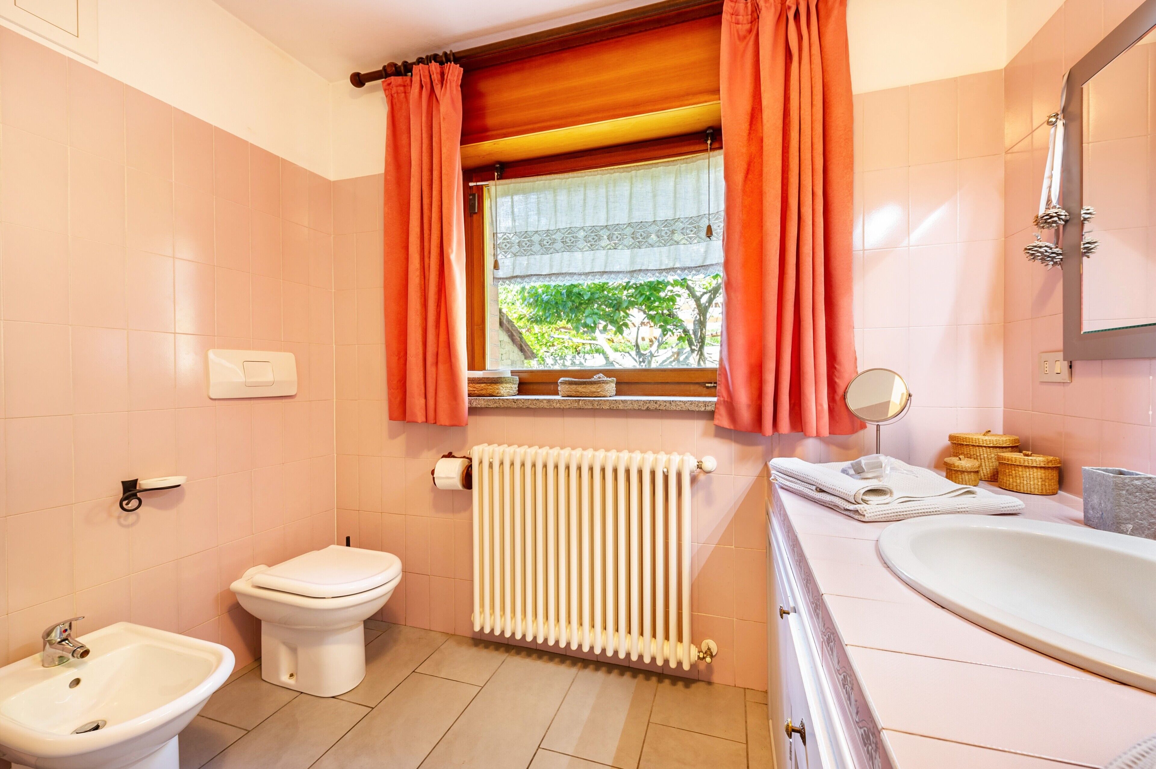 Une salle de bain comprenant des toilettes, un bidet, un radiateur, une fenêtre avec des rideaux et une baignoire.