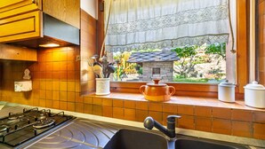 A kitchen with a gas stove, a sink, and a window with a view of a garden and a small building. - Holiday Apartment "Casa Margherita" in Idyllic Location (Aosta)