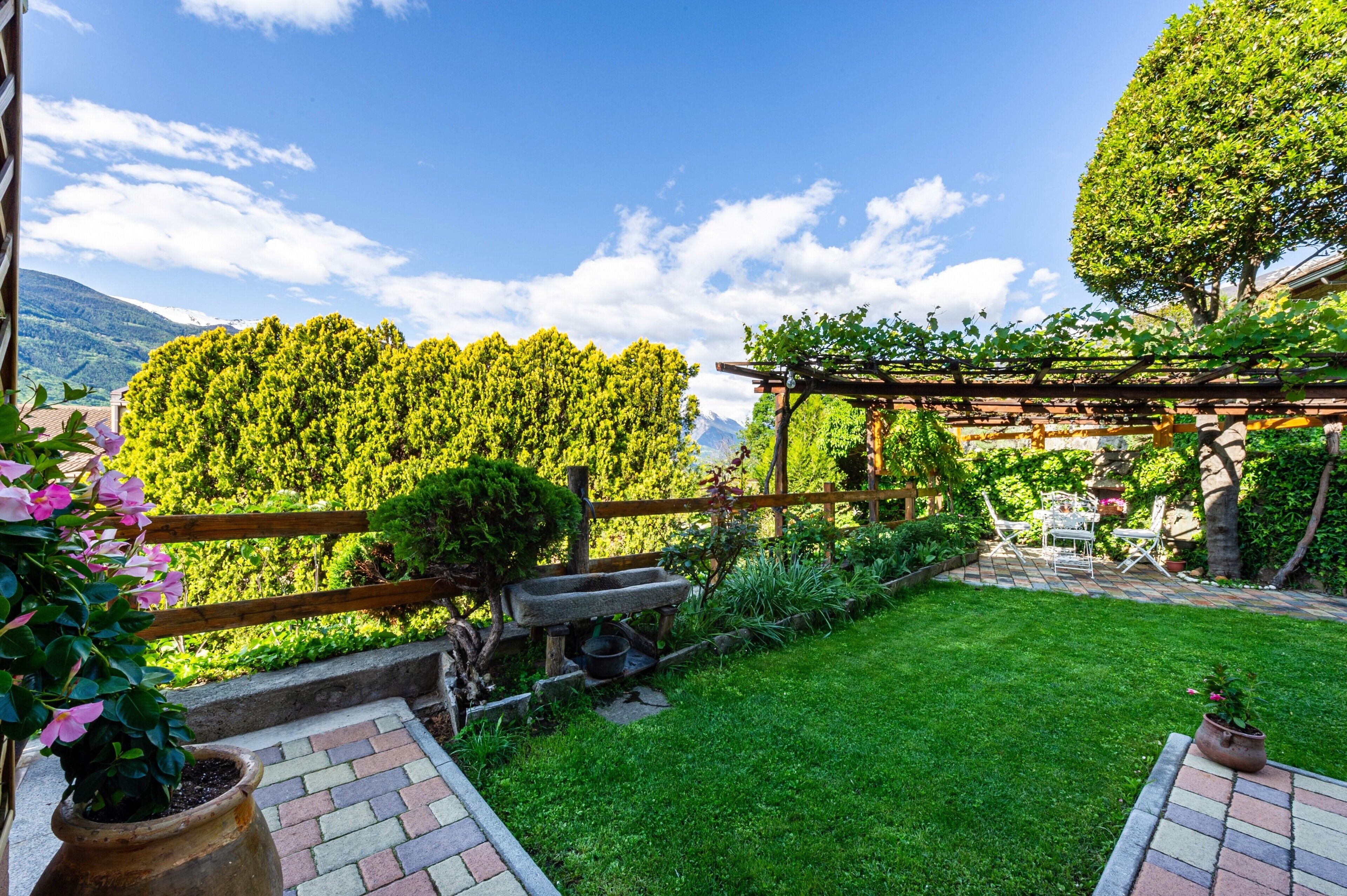 Un jardin agrémenté d’une pergola, d’un banc en pierre et d’une pelouse verdoyante.