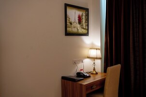 Una camera d'albergo con una scrivania, una lampada, un telefono e un quadro della Torre Eiffel.