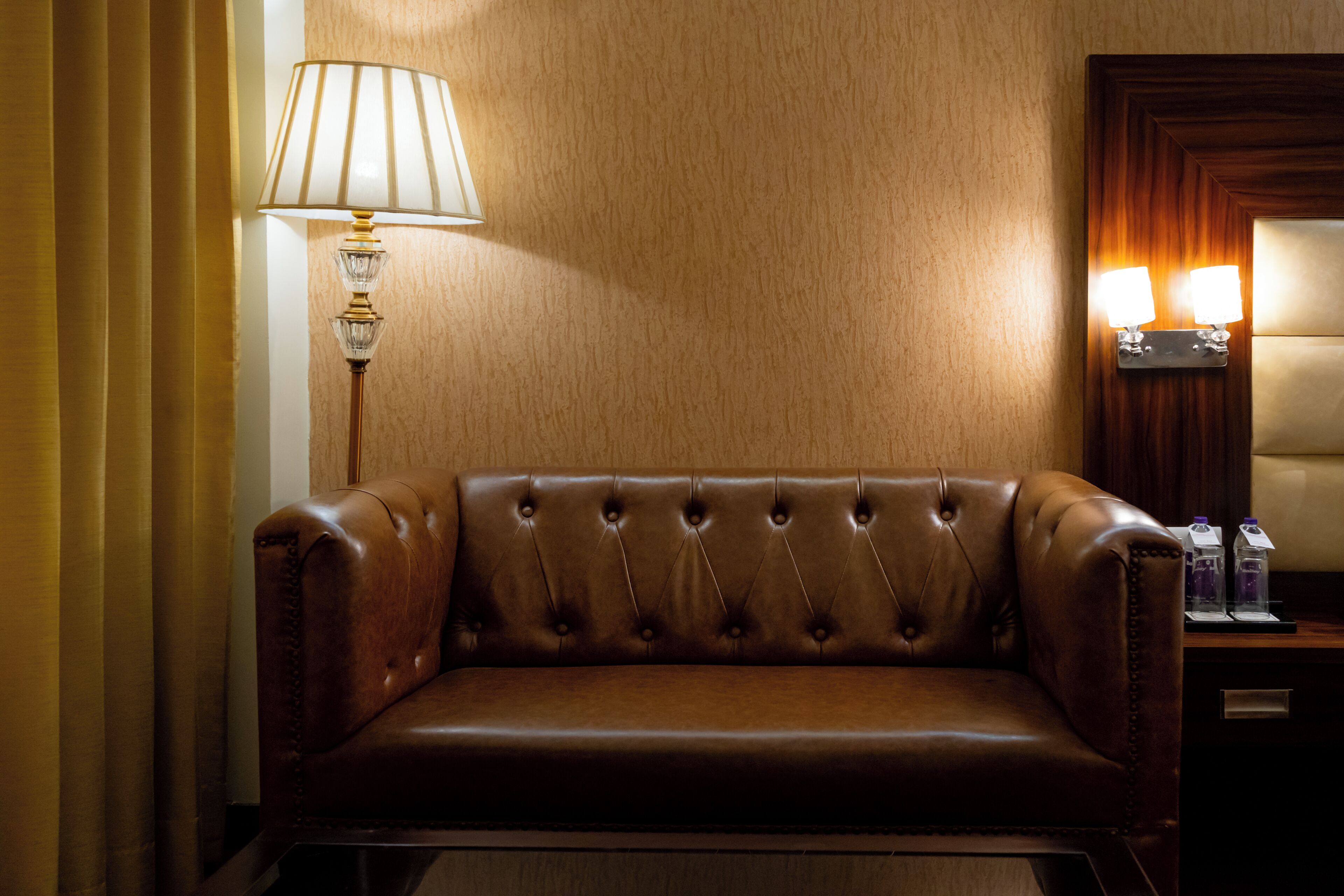 A brown leather sofa in a room with a lamp and a wall-mounted light fixture.