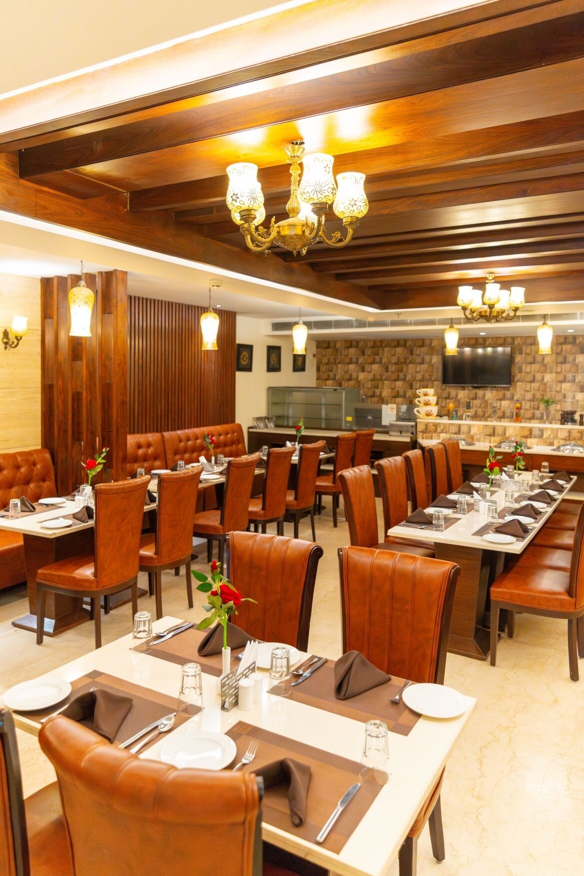 A restaurant with wooden paneling, leather booths, and a modern chandelier. Tables are set with white tablecloths, napkins, and cutlery.