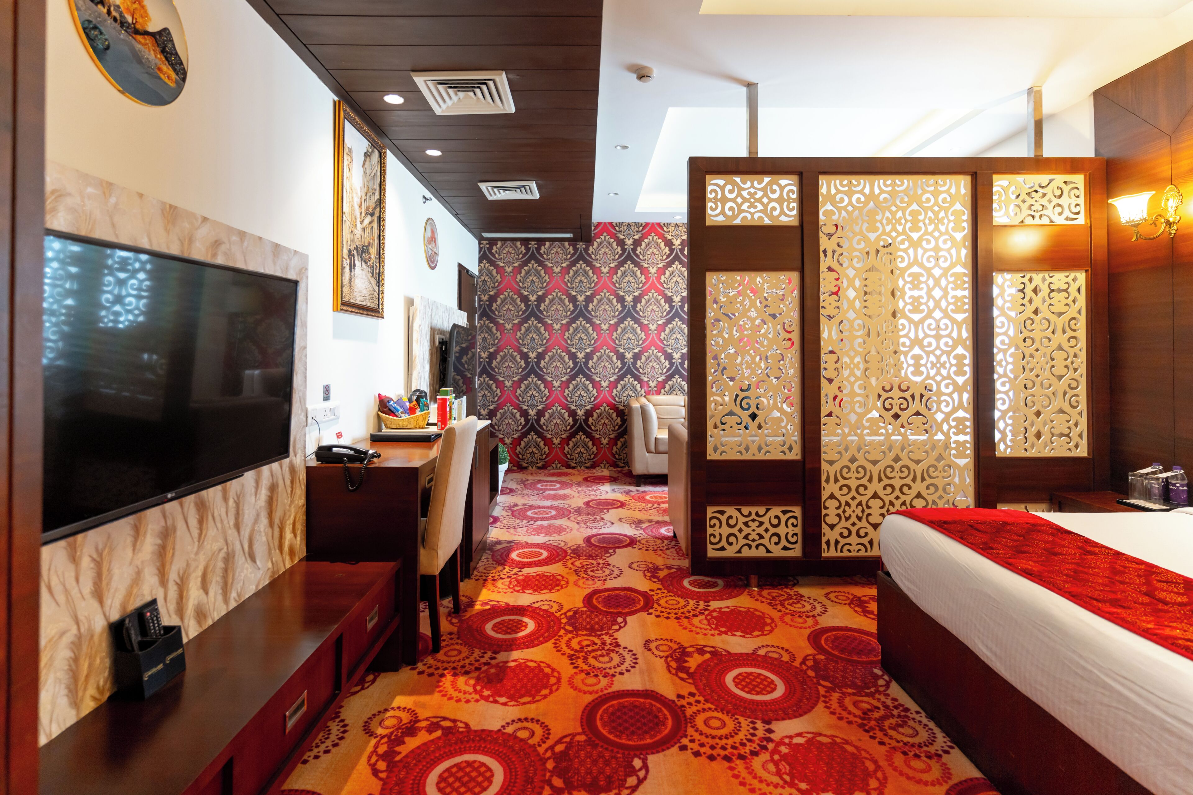 Quarto de hotel com televisão, escrivaninha, cadeira, cama e um separador decorativo.