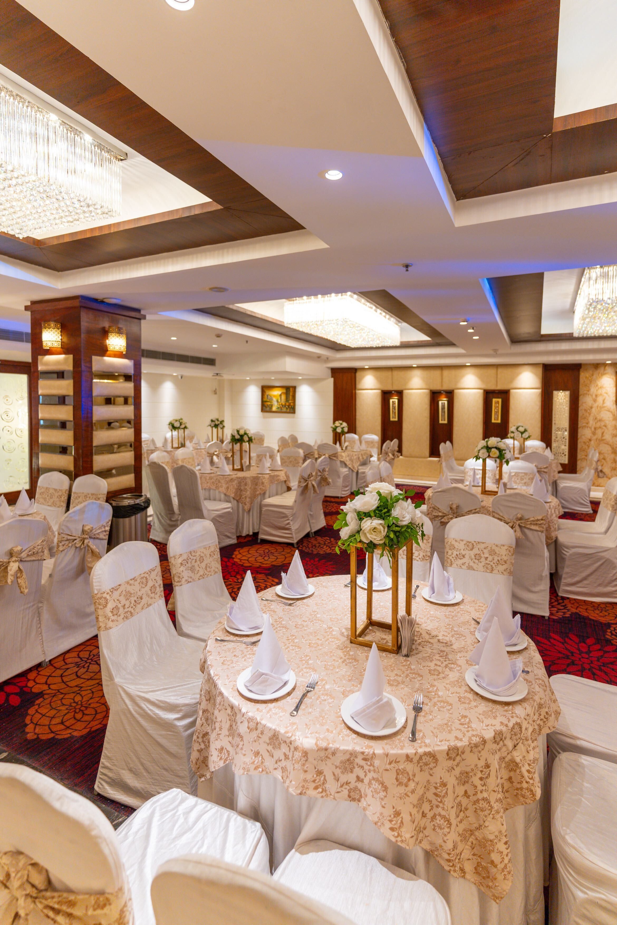 Un salón de banquetes con mesas redondas, manteles blancos y sillas cubiertas de blanco.
