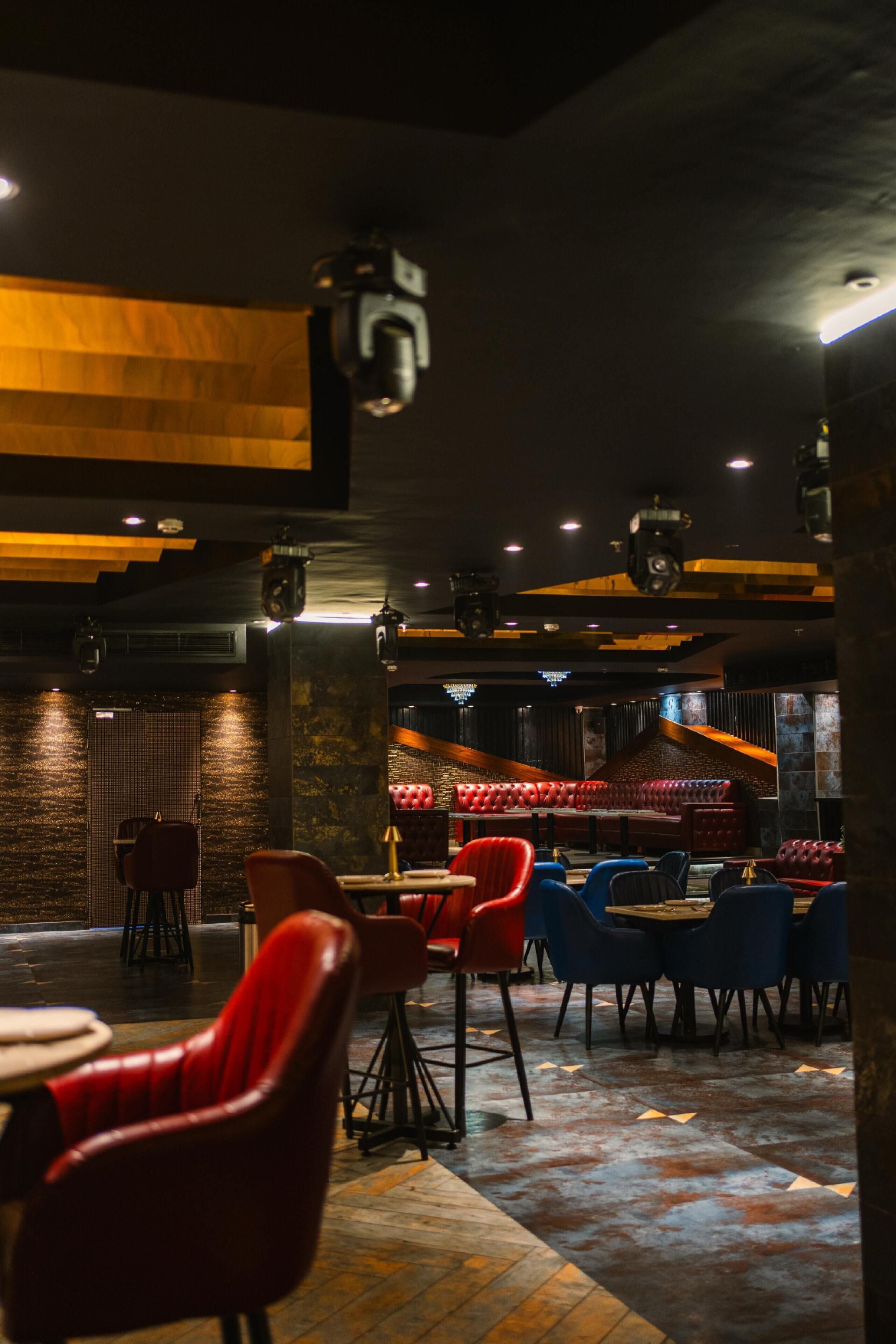 A restaurant with a dark interior, red and blue chairs, and a stage area.