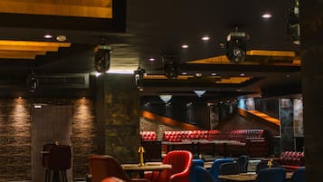 A restaurant with a dark interior, red and blue chairs, and a stage area.