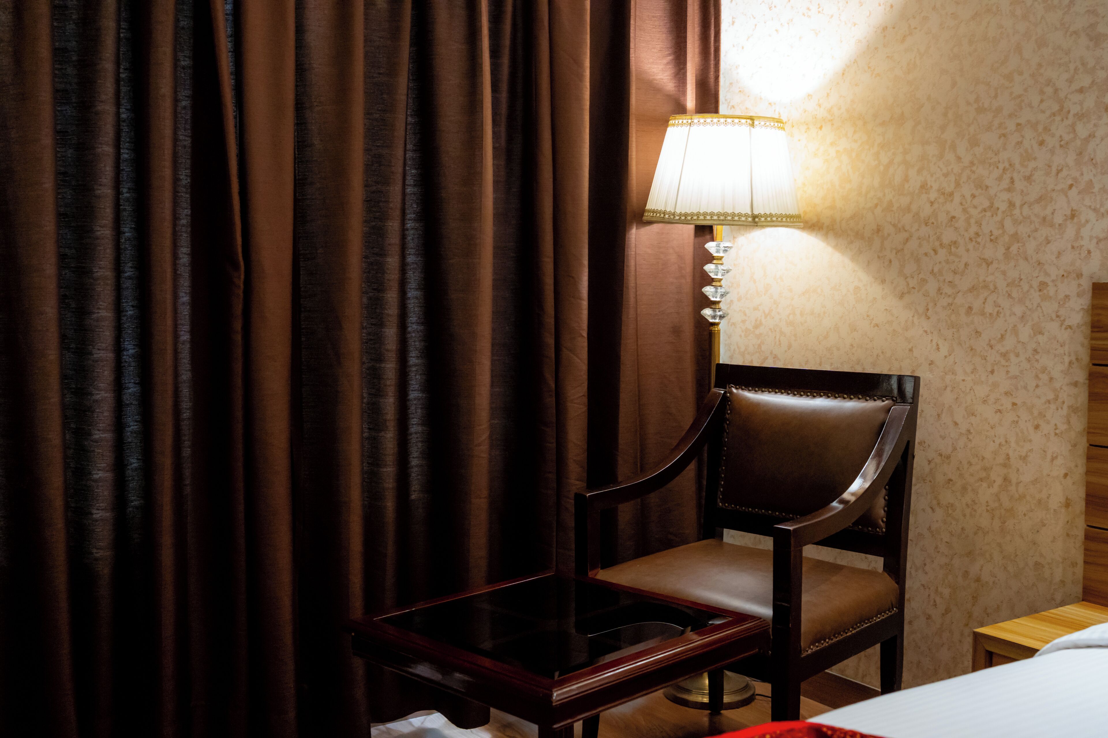 Una habitación de hotel con una silla de madera, una mesita de noche, una lámpara y una cama.