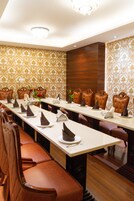 Un salón de conferencias con una larga mesa, sillas de cuero marrón y papel tapiz estampado.