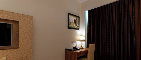 A hotel room with a desk, chair, lamp, picture of the Eiffel Tower, and a window with curtains.