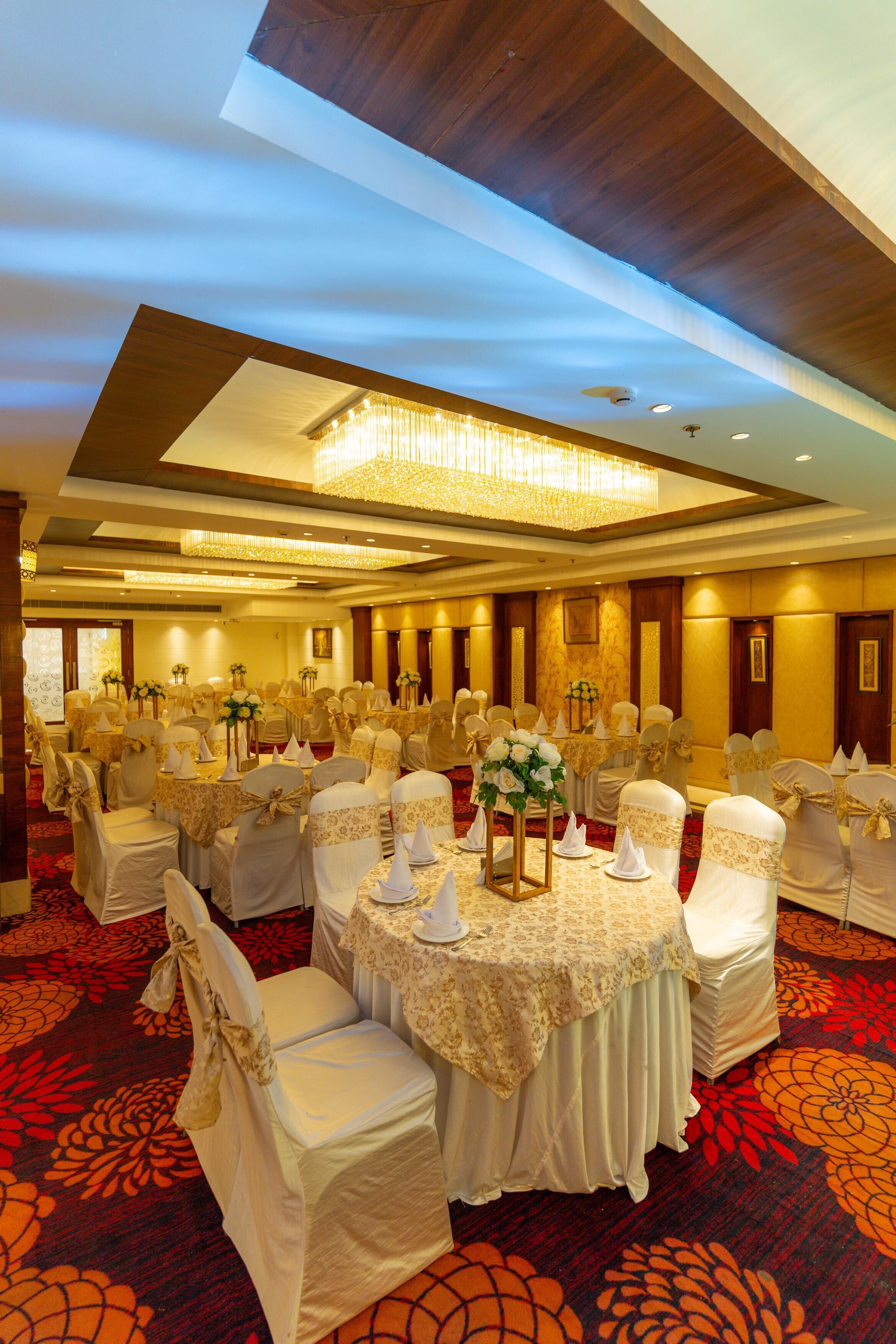 A banquet hall with round tables, white chairs, and floral centerpieces.