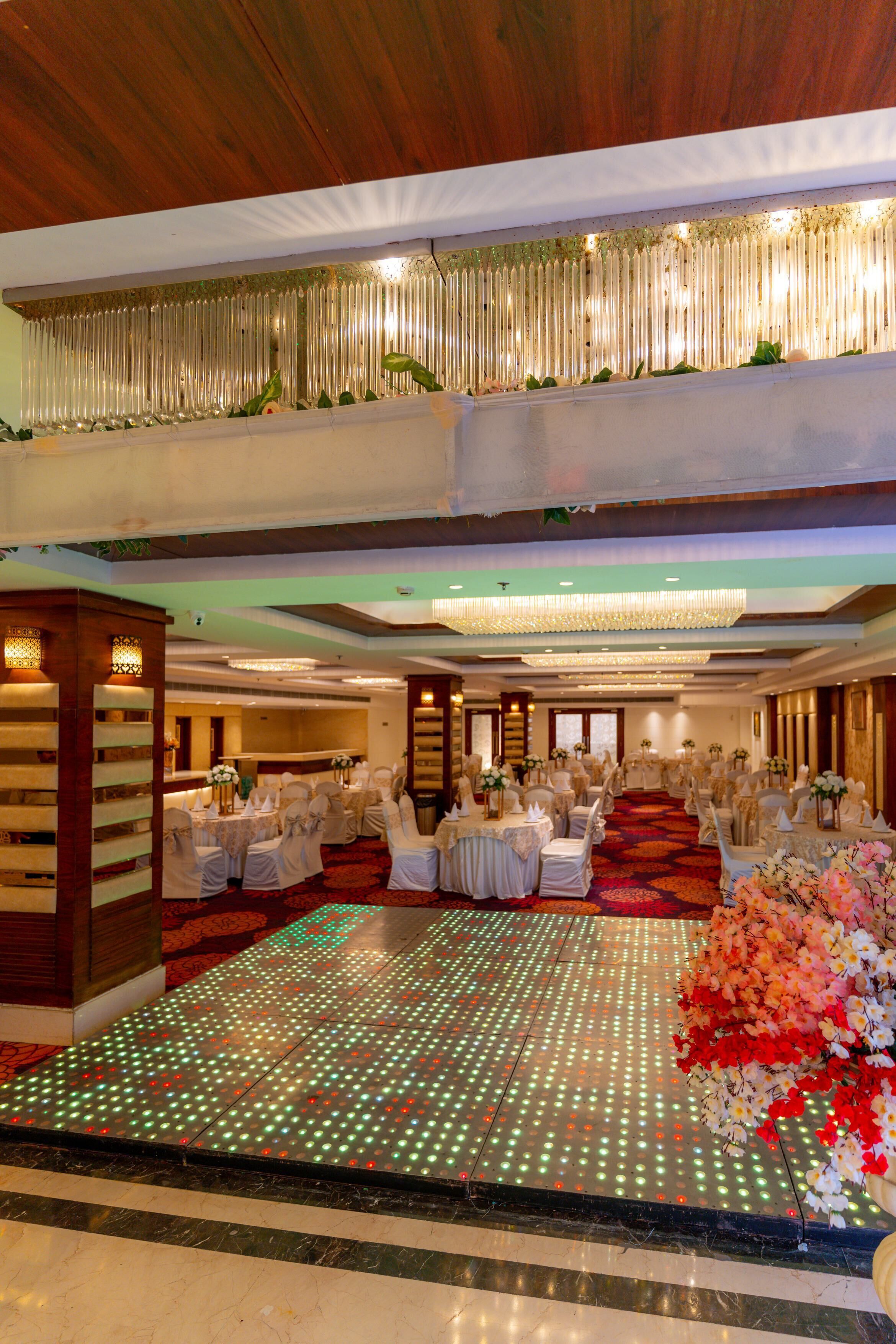 Uma sala de banquetes com assentos em níveis, um salão de dança com luzes de LED e plantas decorativas.
