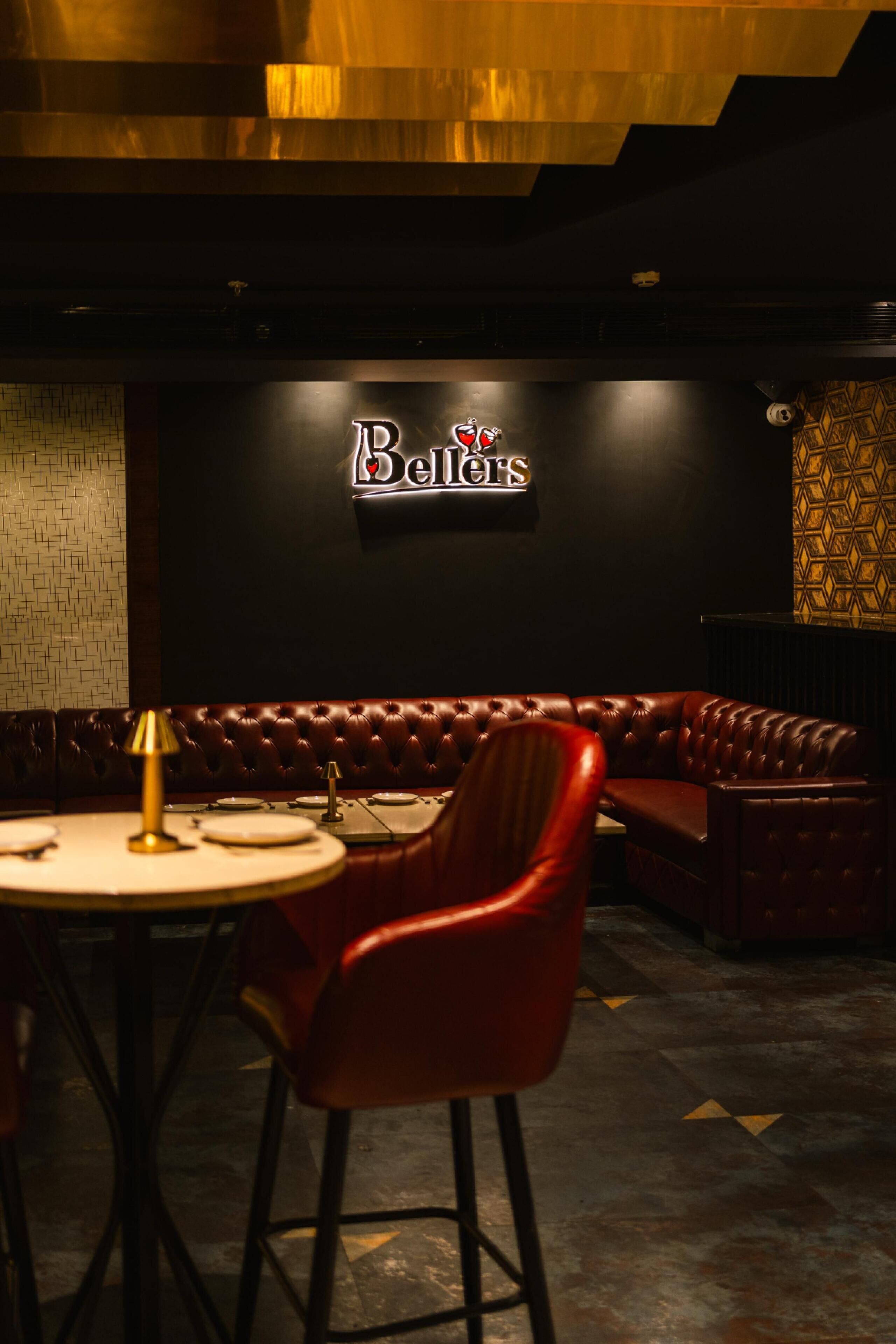 A restaurant interior with a leather booth seating area, a round table with a red chair, and a wall sign that reads 'Bell's.'