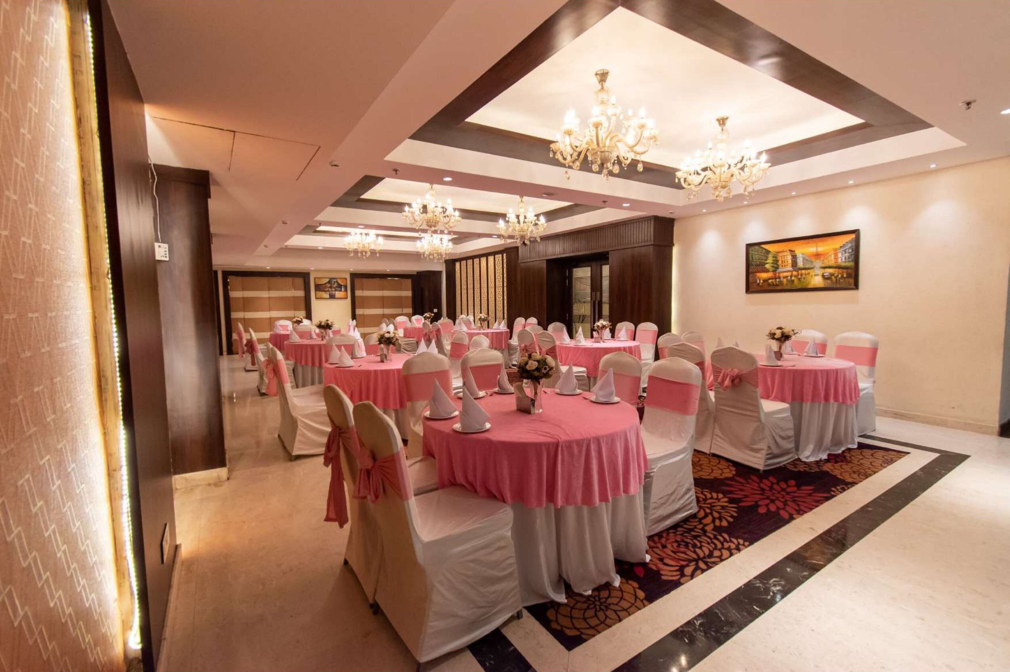 A banquet hall with round tables, white and pink tablecloths, and chandeliers.