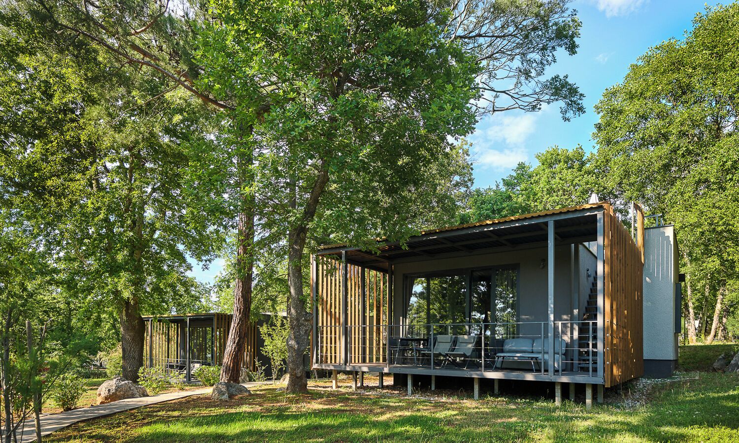A wooden cabin with a covered porch, outdoor seating, and a staircase leading to an upper level.