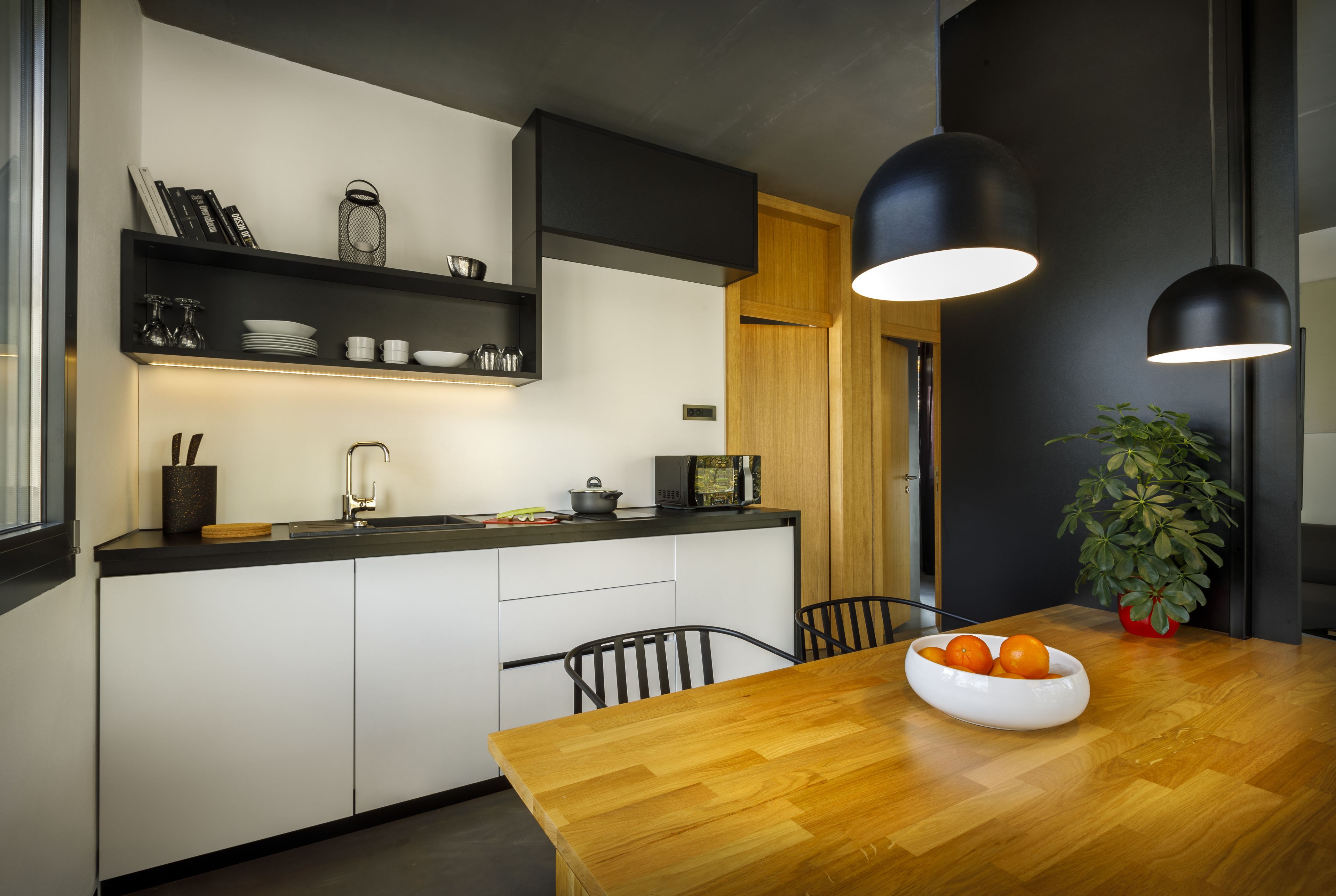Een moderne keuken met een houten eettafel, een schaal fruit en hanglampen.