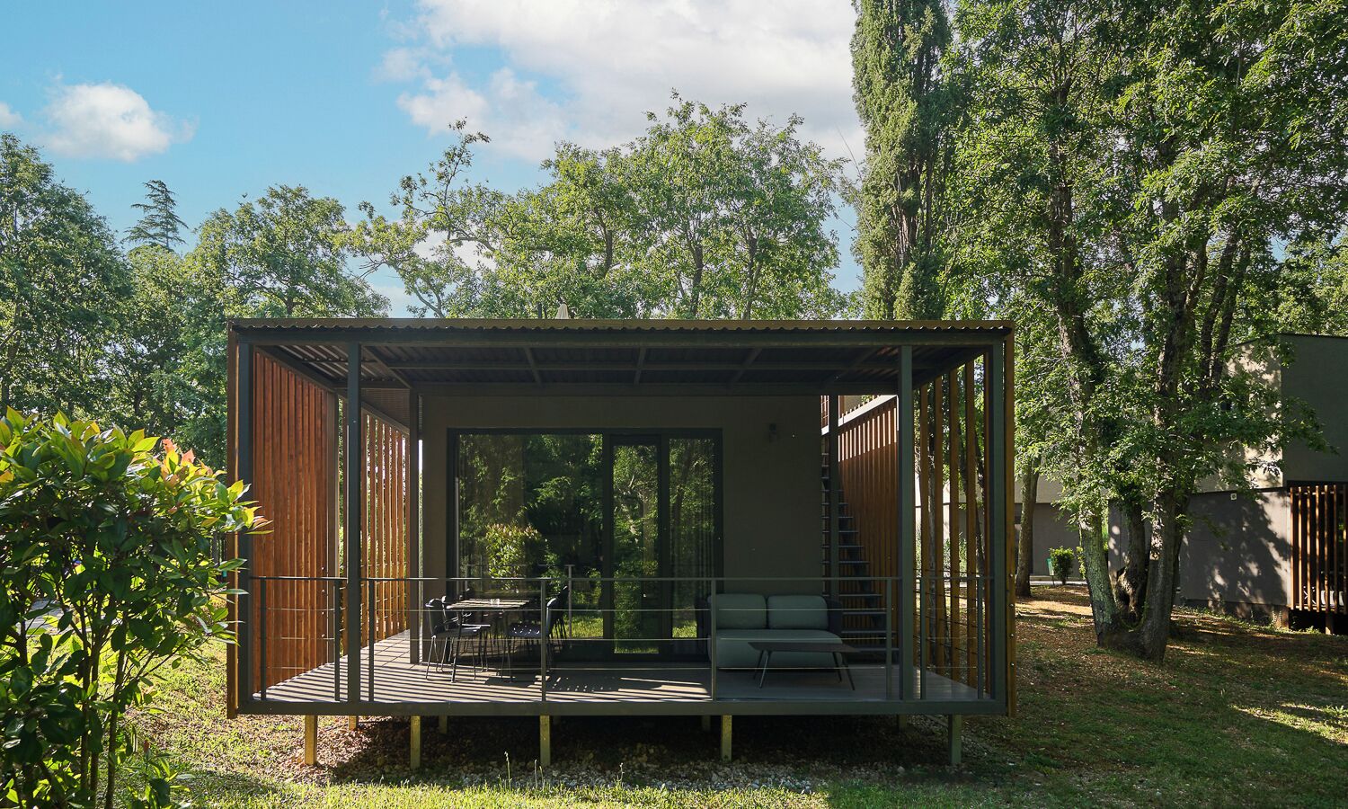 Una estructura moderna y abierta con cerramiento de cristal, una terraza de madera y zonas de estar.