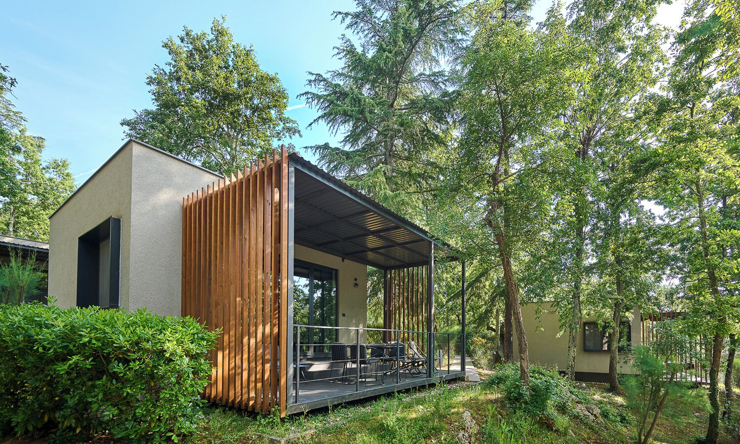 A modern building with a covered outdoor seating area, surrounded by lush greenery.
