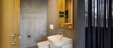 Un baño moderno con puerta de madera, un lavabo blanco, un inodoro y un espejo con repisa superior.