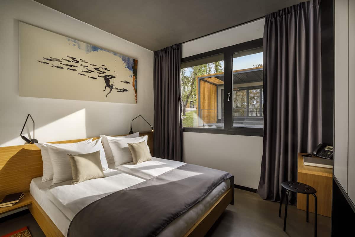 Una habitación de hotel moderna con una cama grande, un escritorio, una silla y una ventana con cortinas.