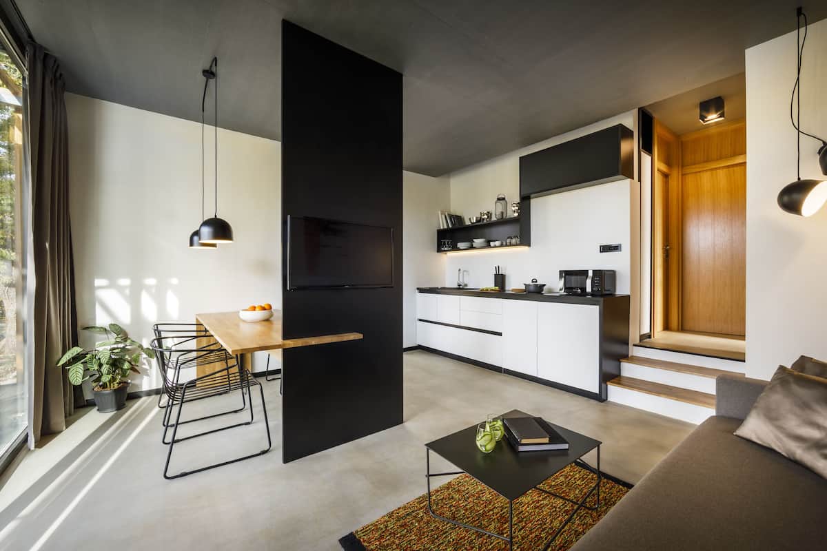 Una cocina moderna con un refrigerador negro, gabinetes blancos y una encimera de madera. Hay una zona de comedor con una mesa y sillas, y un sofá en la sala de estar.