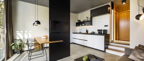 Una cocina moderna con un refrigerador negro, gabinetes blancos y una encimera de madera. Hay una zona de comedor con una mesa y sillas, y un sofá en la sala de estar.