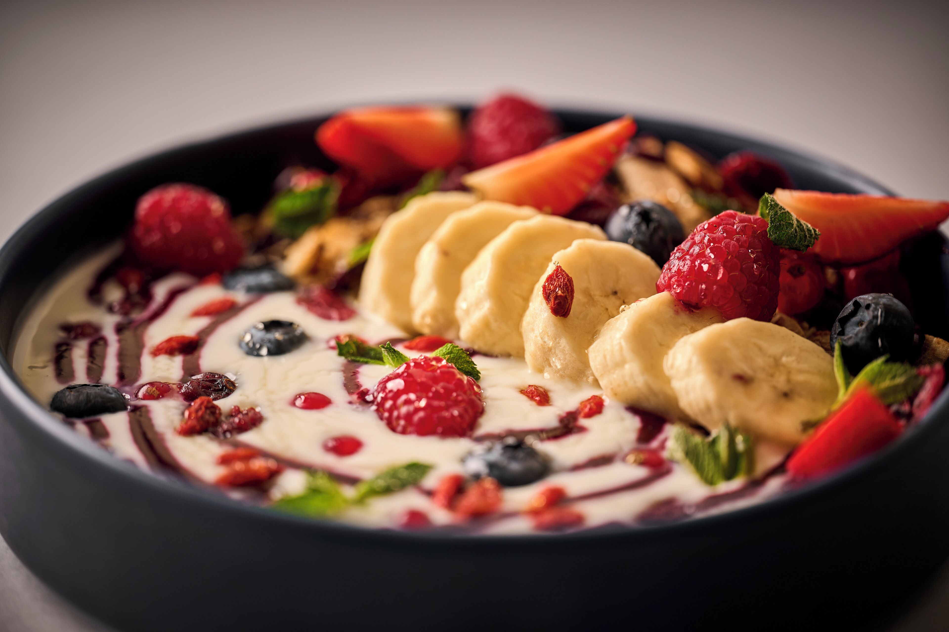 A bowl of yogurt topped with sliced bananas, strawberries, raspberries, and blueberries.
