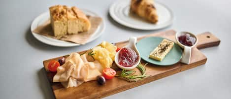 A wooden board with a variety of food items including cheese, tomatoes, olives, and bread.
