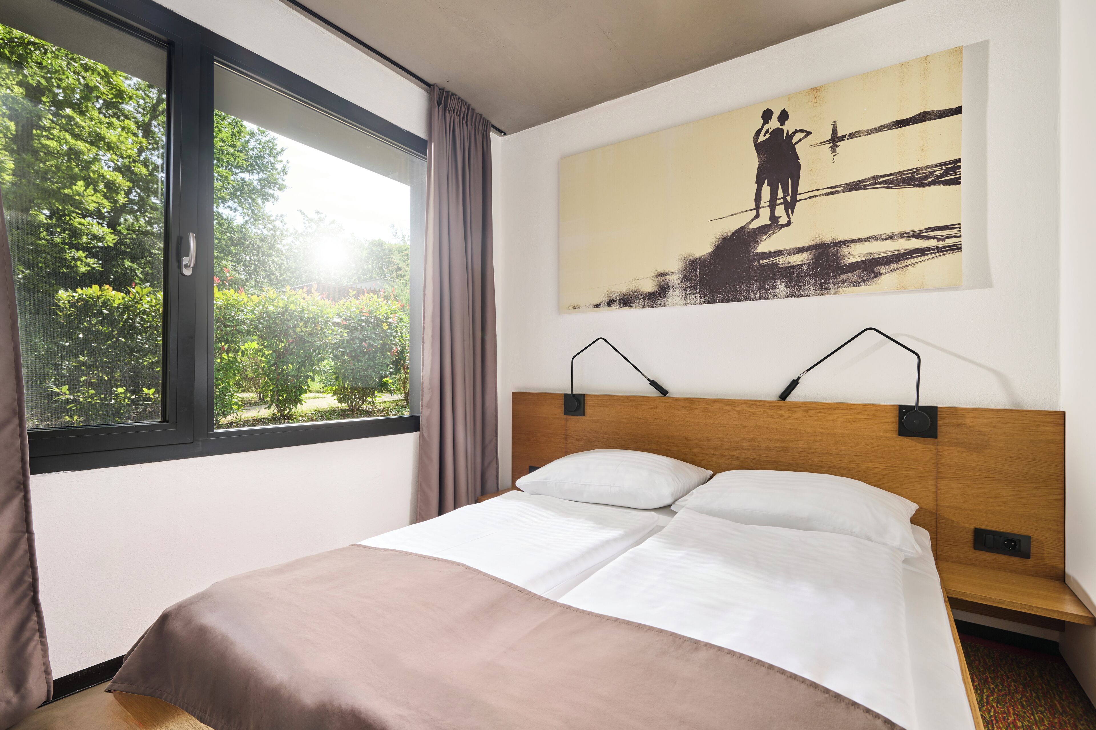 A modern hotel room with a large window, a bed with white linens, a wooden headboard, and a painting of a couple on a cliff.